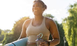 Smiling woman walking with yoga mat and water bottle