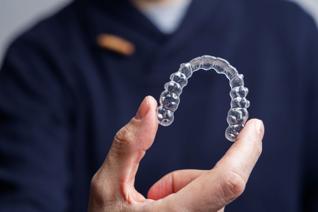 Dentist in dark blue scrubs holding Invisalign with thumb and pointer